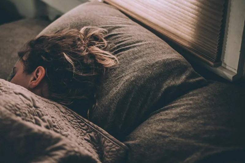 A woman asleep under a grey blanket