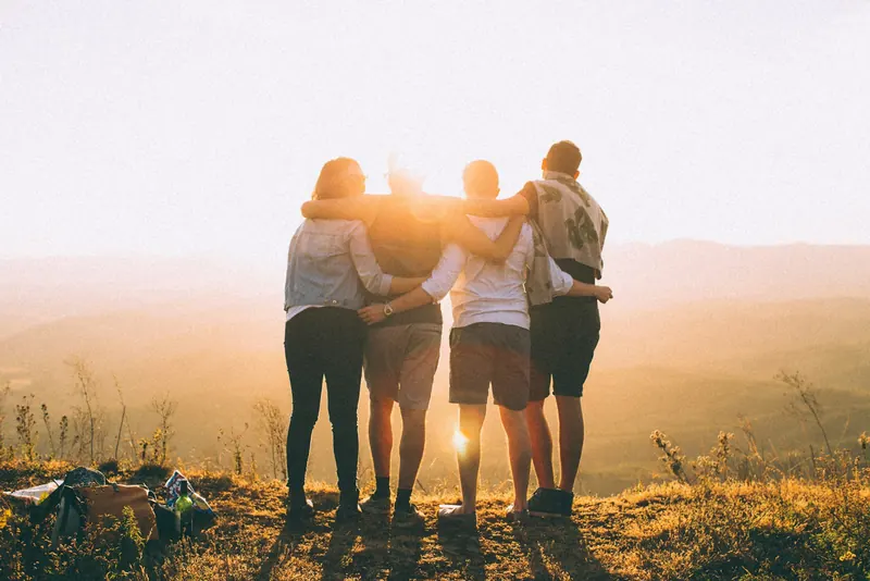 Four friends with their arms around each other, watching a sunset