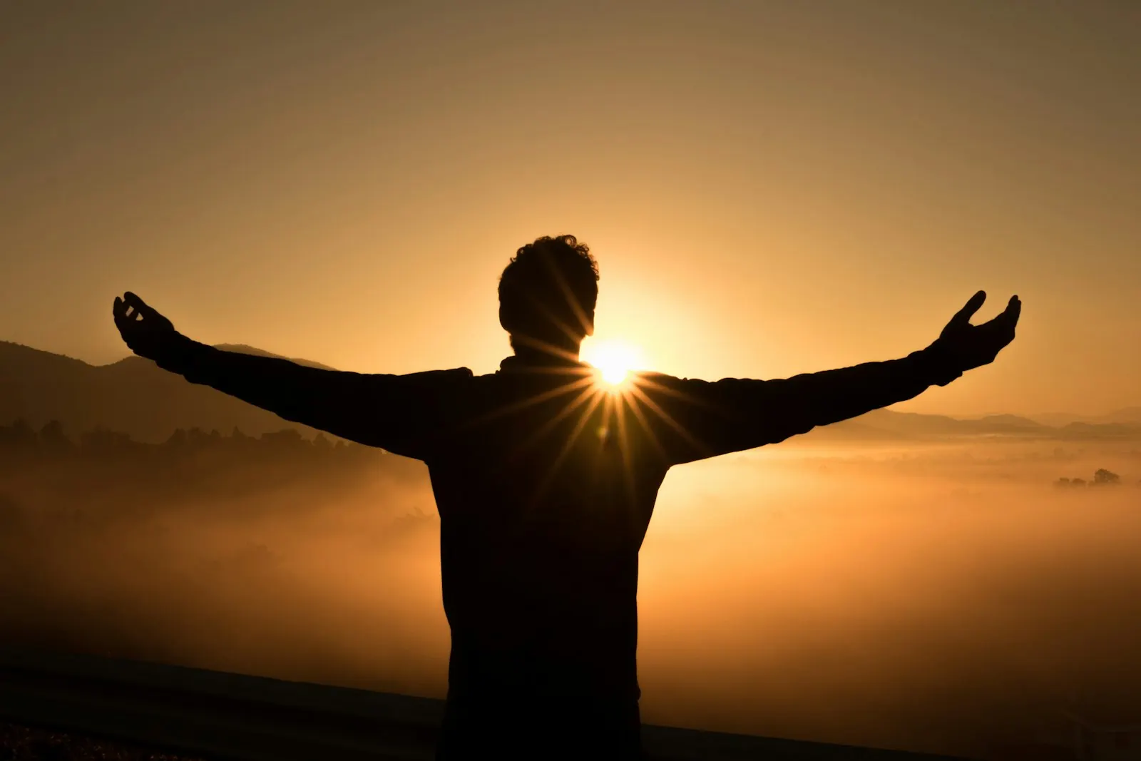 A person with arms open wide facing the sunrise
