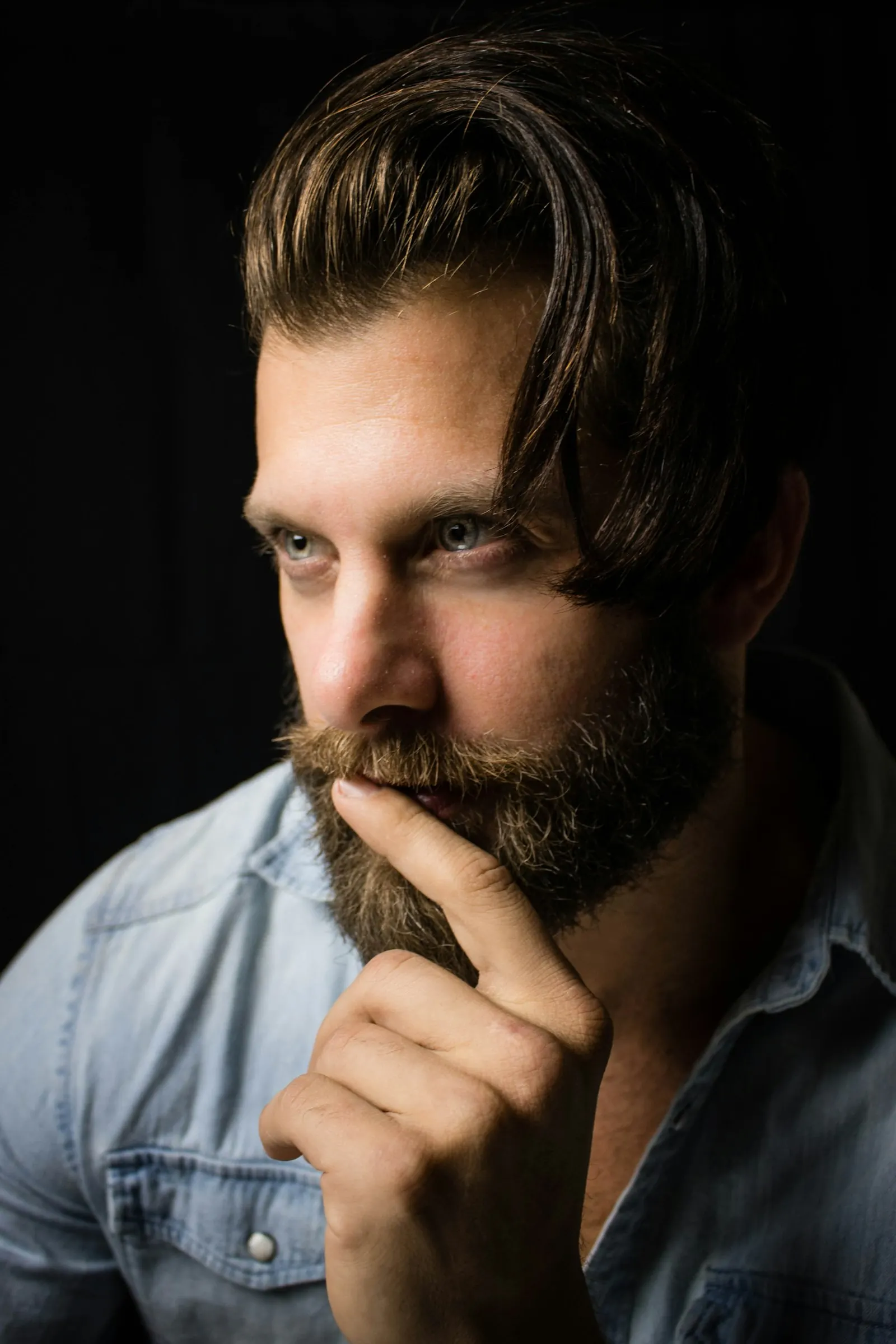 A man resting his chin on his hand, thinking, lit from one side